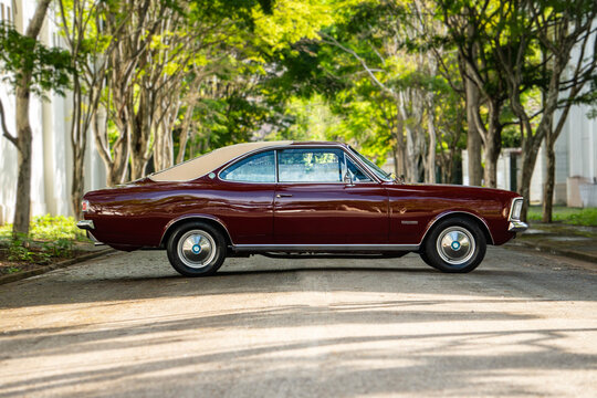 Dark Red Chevrolet Opala full side profile view, Classic vintage coupe parked on tree lined avenue