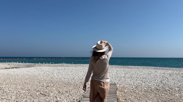 Seguimiento mujer caminando por pasarela de madera hacia el mar