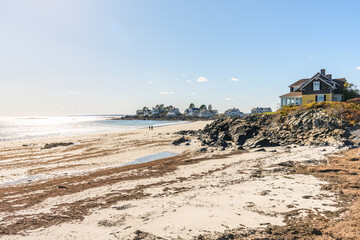 Luxury houses along a sandy beach in Maine on a sunny autumn day. A couple are walking along the shore.