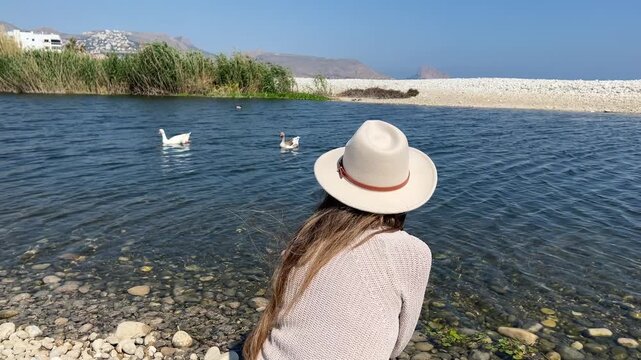 Plano medio trasero mujer sentada a la orilla del humedal con cisnes
