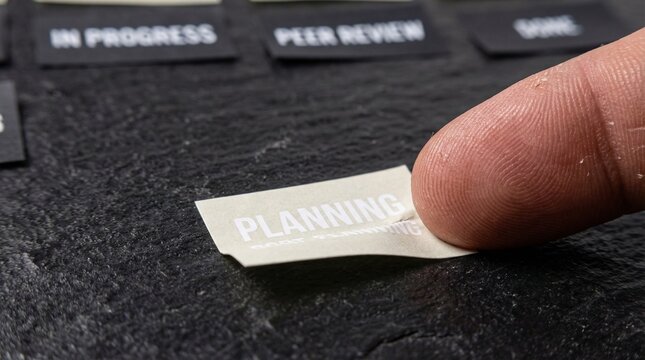 Close-up detail of a hand meticulously peeling a 'PLANNING' sticker from a textured dark surface, symbolizing the crucial first step in project development and strategic workflow management