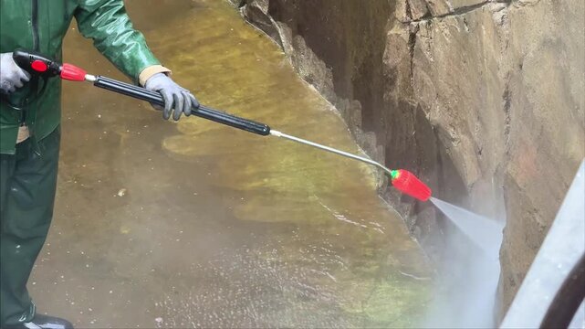 Worker cleaning stone wall with pressure washer removing dirt and algae outdoor