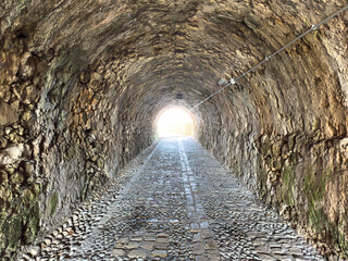 Fototapeta premium Stone tunnel and cobblestone path inside Corfu island New Fortress, Greece. Bright day light at the exit