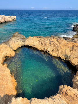 Rocky coastal pool beside turquoise Aegean sea waters, Cyclades islands Greece. Calm sea, summer vacation destination