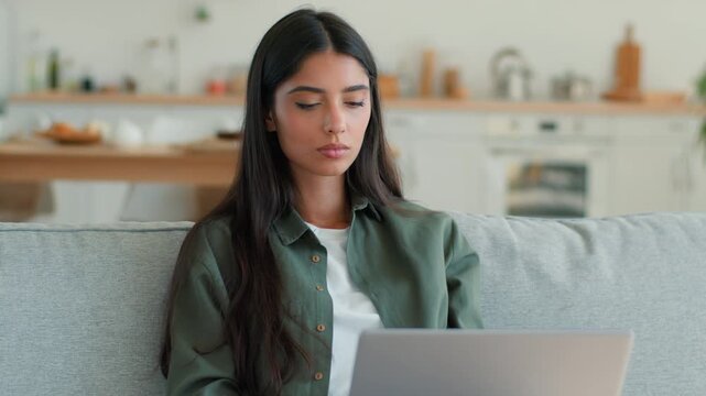 Concentrated Arabian Indian woman working on laptop at home couch focused freelancer student female Hispanic lady typing browsing internet remote work studying online shopping using computer PC indoor