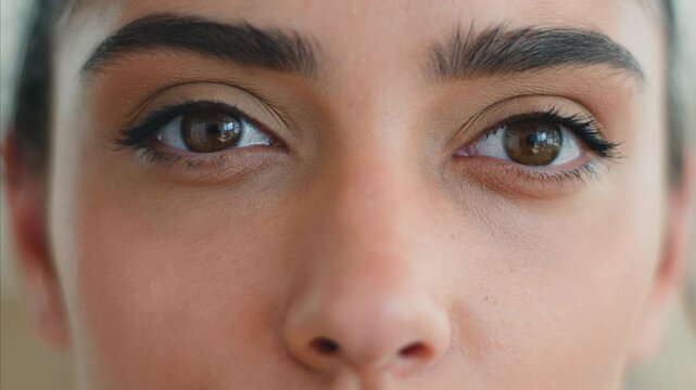 Close up calm Indian woman brown eyes looking at camera with long lashes and eyeliner healthy vision gaze eyesight natural look Arabian Muslim female 20s girl contemplating makeup beauty health indoor
