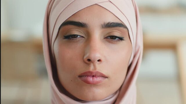 Close up serious calm Muslim woman in pink hijab looking at camera indoors confident ethnic portrait Indian Arabian female Islamic girl headscarf diverse human beauty cosmetology lifestyle expression