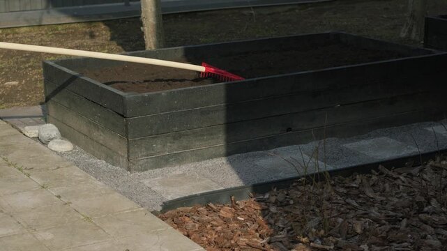 Gardener preparing soil in a raised garden bed with a rake for planting