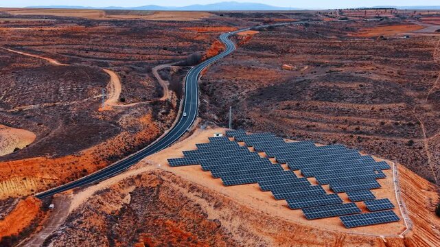 Vast deserted landscape with solar panel field on the hill. Car rides by the highway along the site.