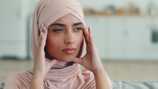Sad frustrated Indian Arabian Muslim woman in hijab thinking holding head indoors female Islamic girl lady feeling sick stressed ill migraine headache pain health problem medicine unwell at home room