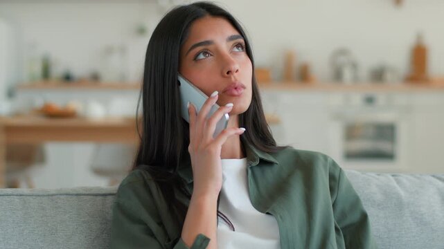 Arabian Indian woman at home sofa talking on mobile phone speaking communicating food delivery or service call Hispanic female girl using smartphone discussing order support calling cellphone indoors