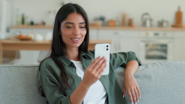 Happy smiling Muslim Arabian woman at home waving hello at webcam during video call talking smartphone greeting online mobile phone chat conference female girl vlog influencer blogger kitchen indoors