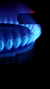 Burning blue flame on domestic gas stove in darkness. Vertical video of energy supply, household utility usage, and natural fuel consumption, indicating a cooking process, culinary inspiration