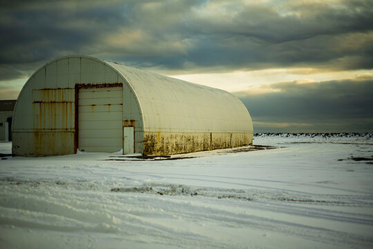 Weathered Rusty Quonset Hut in a Snowy Field Under a Dramatic Sky