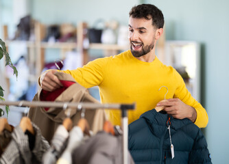 Young man buyer choosing down jacket or raincoat in clothing store © JackF