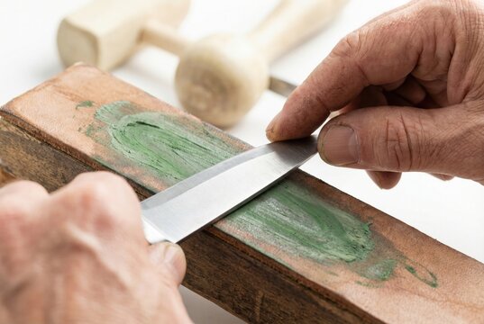 Craftsman sharpening the edge of a steel knife on a leather strop with green polishing compound