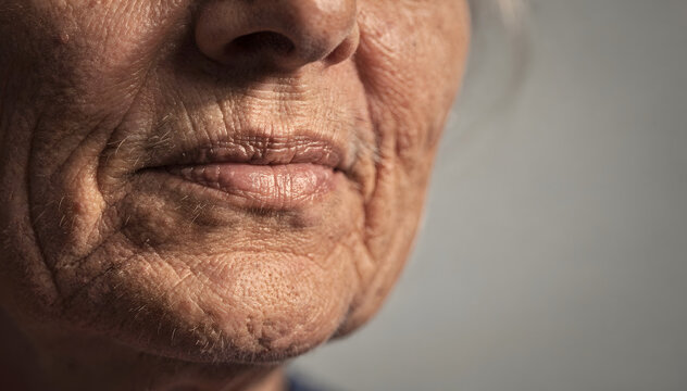 Close-up of an elderly person's mouth and jawline, revealing intricate wrinkles and a lifetime of expression, with soft, natural lighting on a neutral background