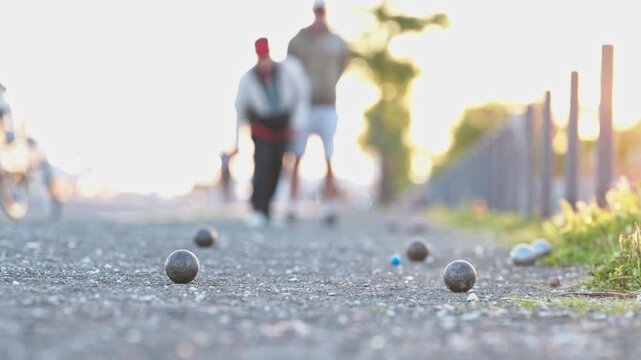People playing petanque throwing a metal boule during sunset