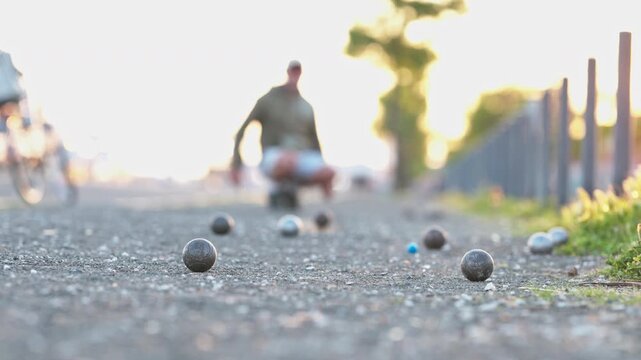 Person playing p tanque throwing a boule at sunset