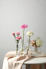 Fototapeta premium Beautiful flowers in vases on white table against light background