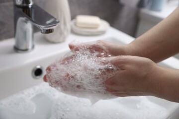 Fototapeta premium Woman washing hands with soap near white sink in bathroom, closeup