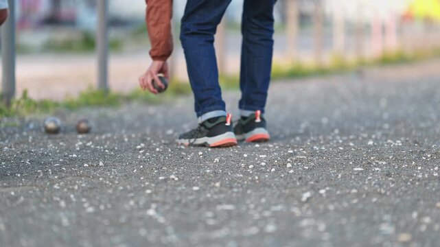 Person picking up metal ball during petanque game