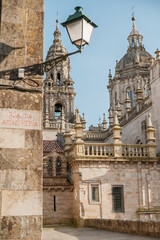 Obraz premium Santiago de Compostela Cathedral baroque towers and dome visible above a historic stone street with an old street lamp. Capturing the ancient architecture and pilgrim city atmosphere under a clear sky