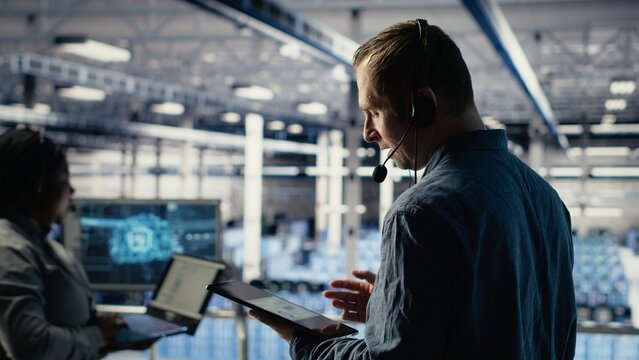 Data center admin talking in audio headset mic, helping clients resolve website hosting problems. Server farm worker on industrial platform helping users keep online services running, camera B