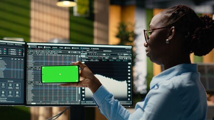 Prop firm intern in office learns new trading strategies from video lesson on green screen mobile phone. Brokerage company trainee using chroma key smartphone to watch educational content © DC Studio