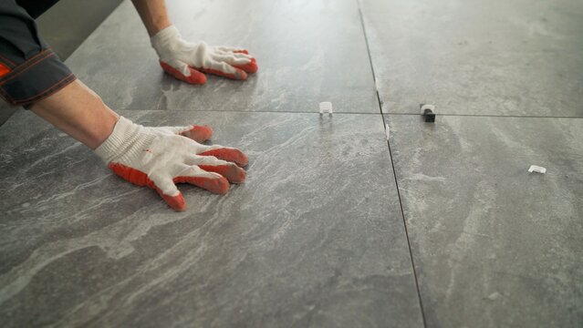 Close up of a construction worker installing large format ceramic tiles on a floor. Using a tile leveling system for a professional finish. Home renovation and interior design concept.