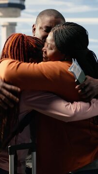 Vertical Video Bittersweet goodbye between parents and teen daughter in busy airport terminal, heartfelt embrace and supportive send-off. Young traveler exchange student flying overseas, proud sad