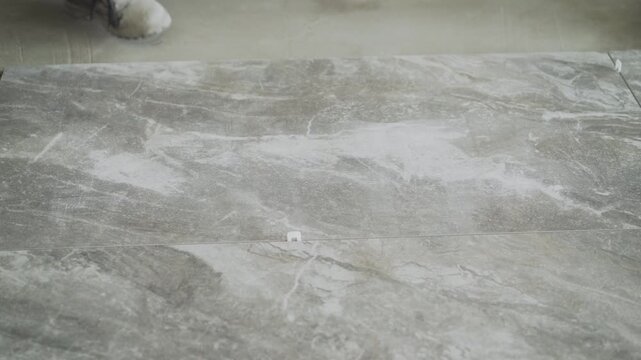 Close up of a construction worker installing large format ceramic tiles on a floor. Using a tile leveling system for a professional finish. Home renovation and interior design concept.
