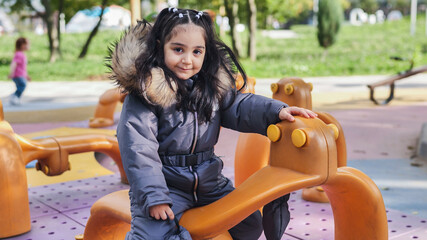 Cute child playing in playground wearing warm winter jumpsuit with fur hood © Довидович Михаил