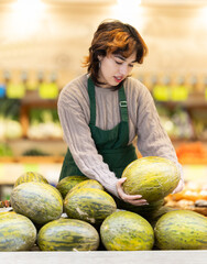 Fototapeta premium Seller in grocery vegetable shop arrange melon. Girl creates stock of fruit in display, forms showcase. Vegetable shop near house. Organic vegetable shop offer assortment, business case