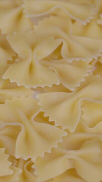 Closeup of dried bowtie pasta grains. Pile of warm beige uncooked ribbonshaped pasta slices. Detailed view of arranged dry farfalle pasta with serrated edges in warm tones