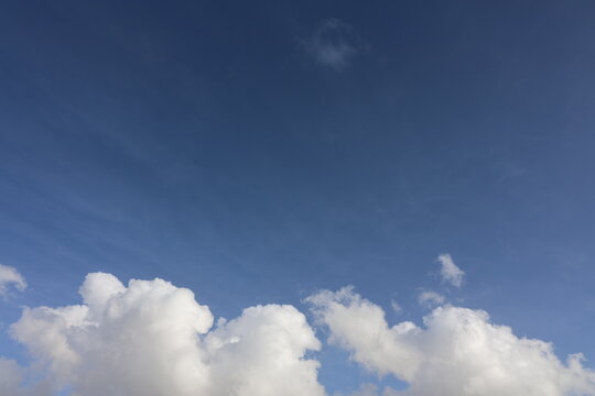Beautiful blue sky with white fluffy cumulus clouds. Summer day background. High resolution nature texture suitable for wallpaper or design overlays