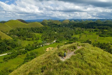 Fototapeta premium Aerial view of the Chocolate Hills from the free viewpoint in Batuan, Bohol. Iconic conical limestone formations covered in green grass under a cloudy sky, Philippines.