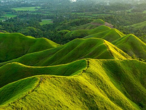 Aerial sunrise over Alicia Panoramic Park, Bohol. Rolling green ridges of Binabaje Hills under golden light, scenic tropical mountain landscape in the Philippines.