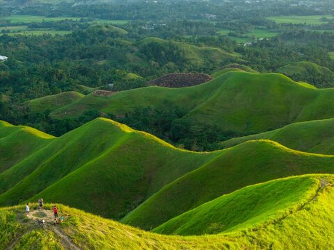 Aerial sunrise over Alicia Panoramic Park, Bohol. Rolling green ridges of Binabaje Hills under golden light, scenic tropical mountain landscape in the Philippines.