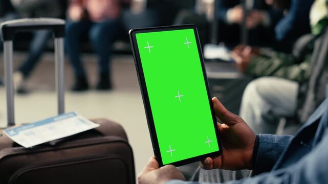 Vertical chroma key tablet in international airport terminal with diverse passengers relaxing in waiting lounge. Travelers with suitcases checking passports and plane tickets before journey.