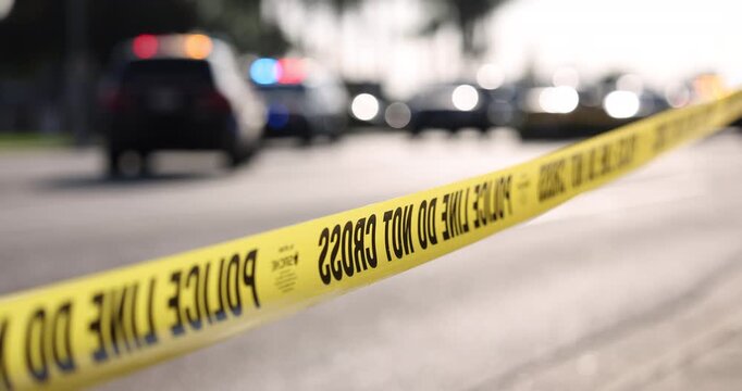 Daytime abstracted view of cordon tape and police units responding to an emergency.