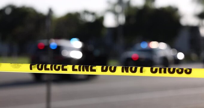 Daytime abstracted view of cordon tape and police units responding to an emergency.