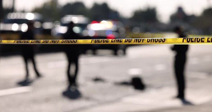 Cordon tape blocks off a day time emergency scene with an abstracted police car in the background.