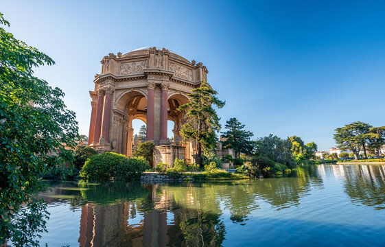 A serene morning view of the Palace of Fine Arts rotunda reflecting in the tranquil lagoon under a clear San Francisco sky.
