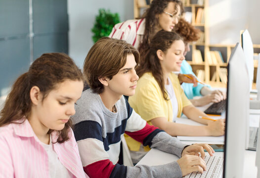 Student teacher teenagers in classroom with computers. Focused students learn coding together as the instructor guides teamwork and provides training. Clear concept of digital education.