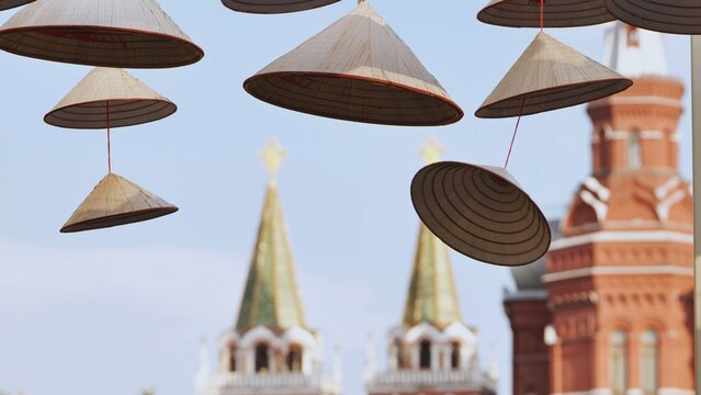 Traditional Asian conical hats hanging outdoors with a red brick historic tower in the background.