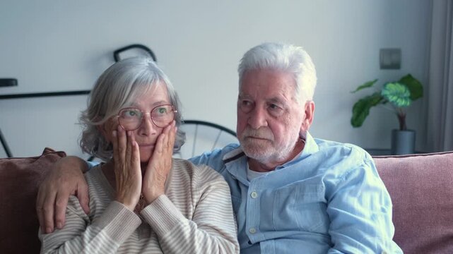 A senior man embraces his gray woman, offering gentle reassurance as they sit together in their home interior, sharing authentic sentiment and pensive mood.