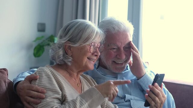 A joyful senior couple celebrates exciting news while looking at a smartphone at home. They express happiness and surprise, sharing a moment of triumph and connection using modern technology.