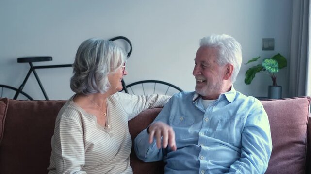 Happy senior couple relaxing on a couch, sharing a loving moment, laughing and embracing. Their strong bond and affection are clearly visible, showcasing enduring love and companionship in retirement.