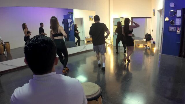 Dancers are dancing salsa in front of a mirror while a musician plays the congas in dance class